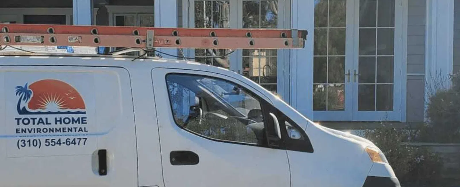 White utility van with ladder parked outside a modern gray house with large windows and white trim.