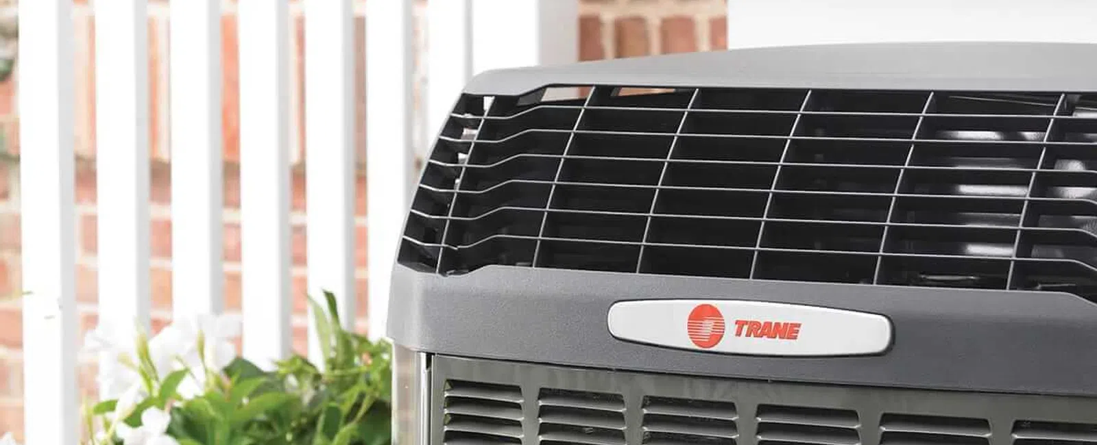 Close-up of a Trane air conditioning unit outdoors with greenery and brick wall background