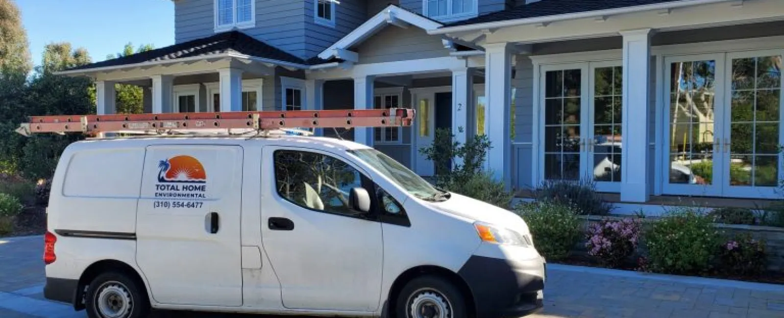 White Total Home Environmental service van parked in front of a modern two-story gray house with large windows.