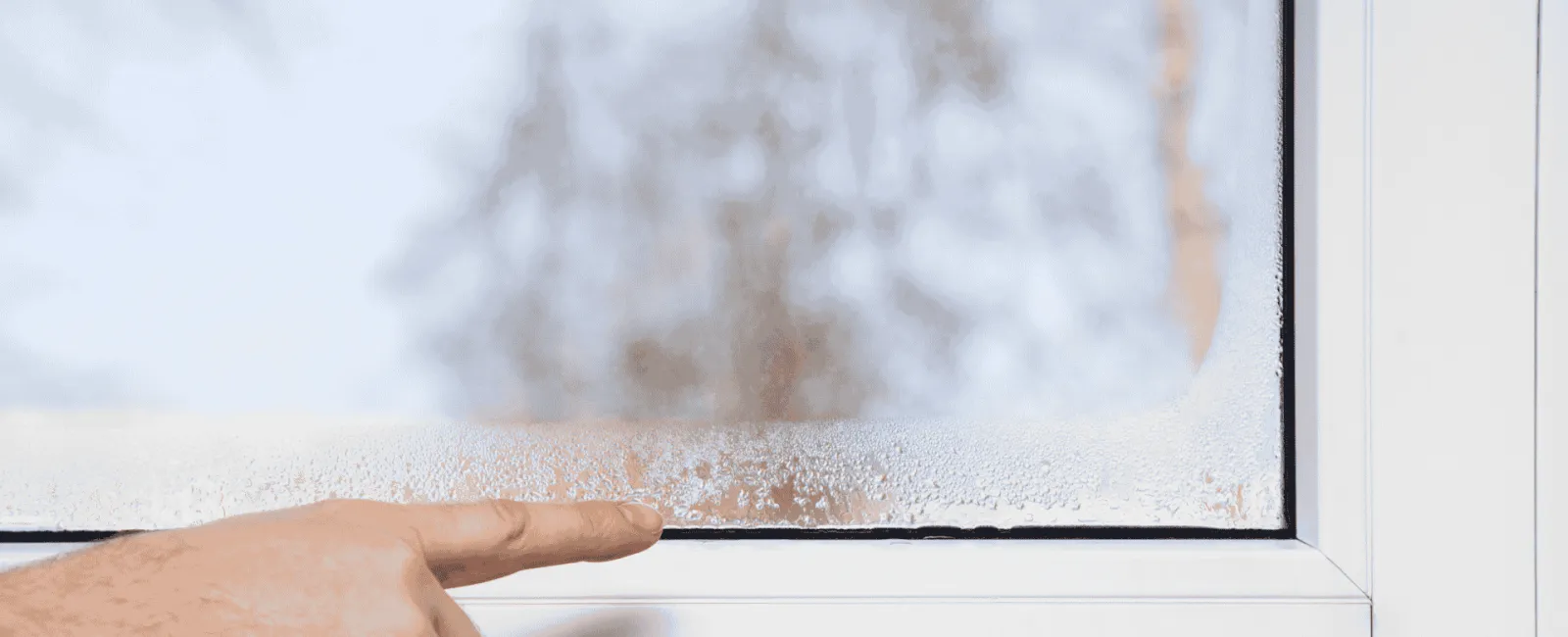 Hand pointing at condensation on a window pane from humidity