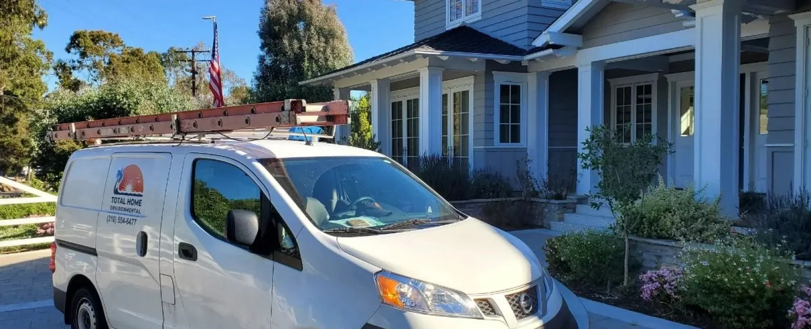 White service van with ladder on roof parked outside modern two-story house on sunny day