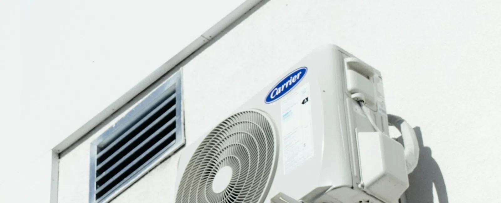 White Carrier air conditioning unit installed on a white building wall under a clear blue sky.