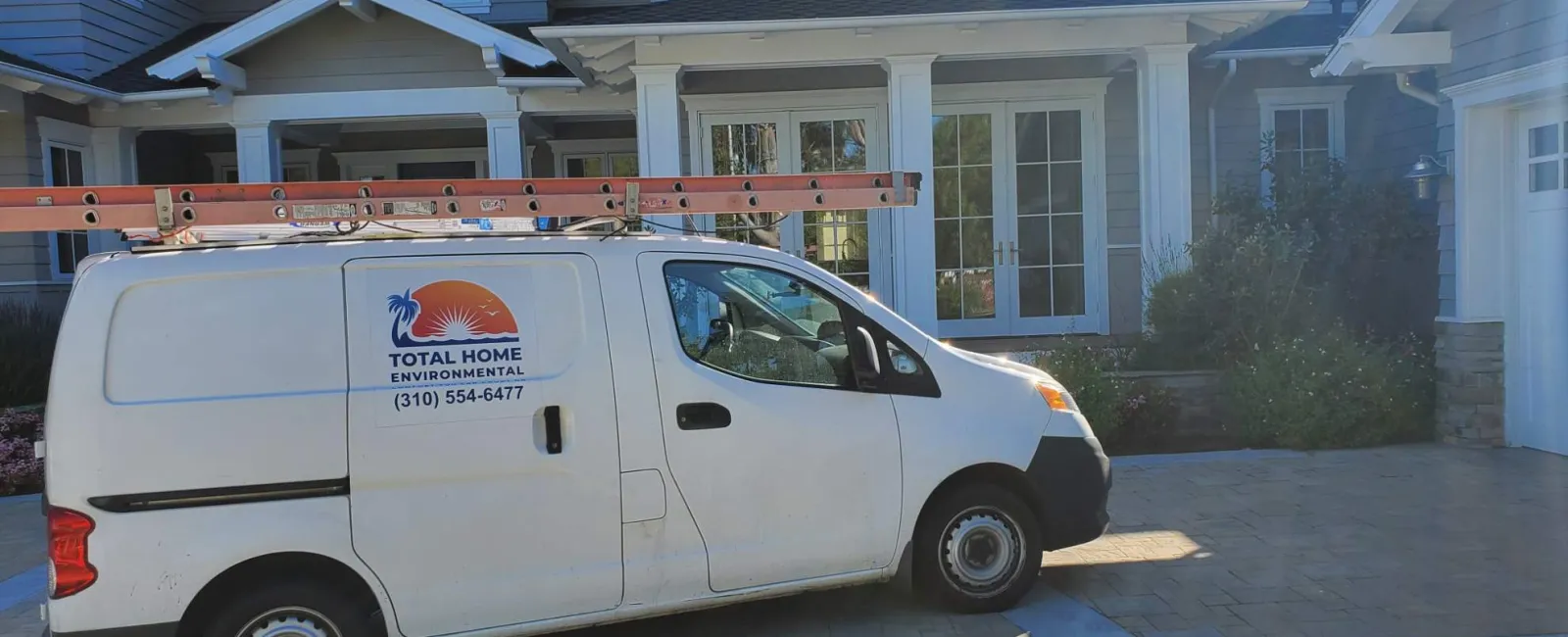 White service van with ladder parked in driveway of large gray two-story house with white trim and columns