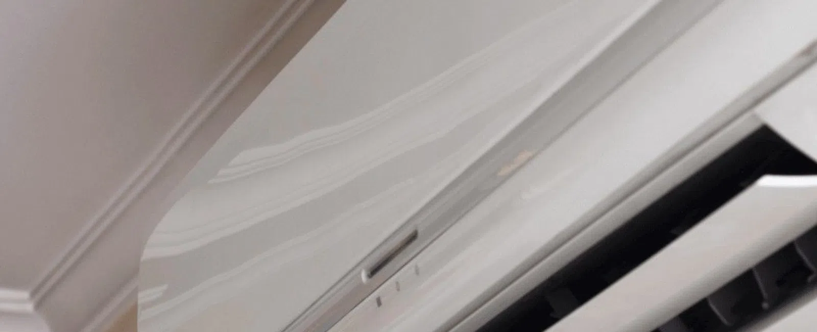 Modern white wall-mounted air conditioner unit installed near ceiling for indoor cooling.