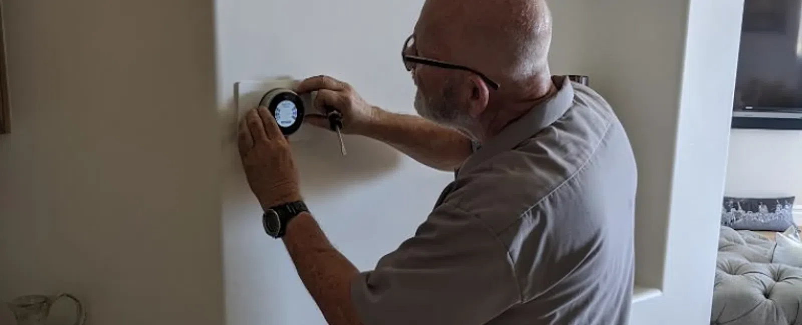Elderly man adjusting a modern smart thermostat on a white wall in a cozy living room.