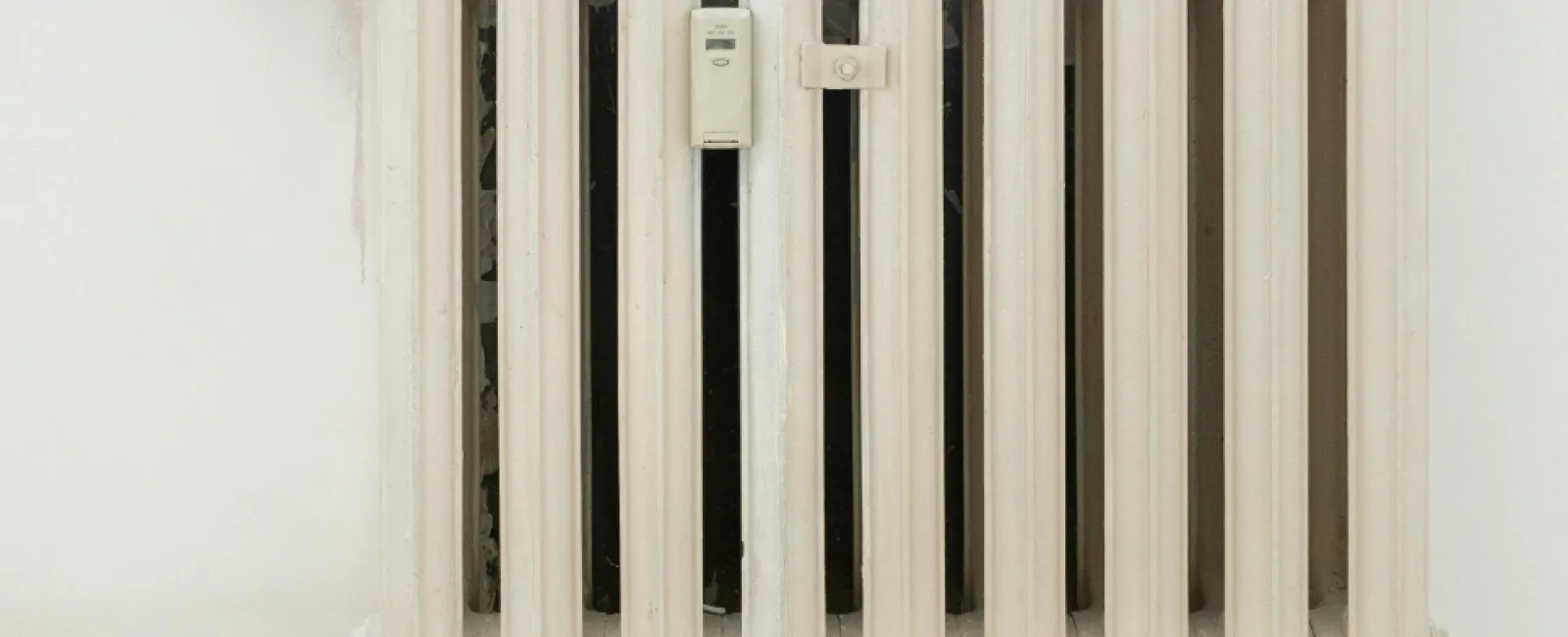 White vintage cast iron radiator heater mounted on a white wall with pipe connections and a control valve.