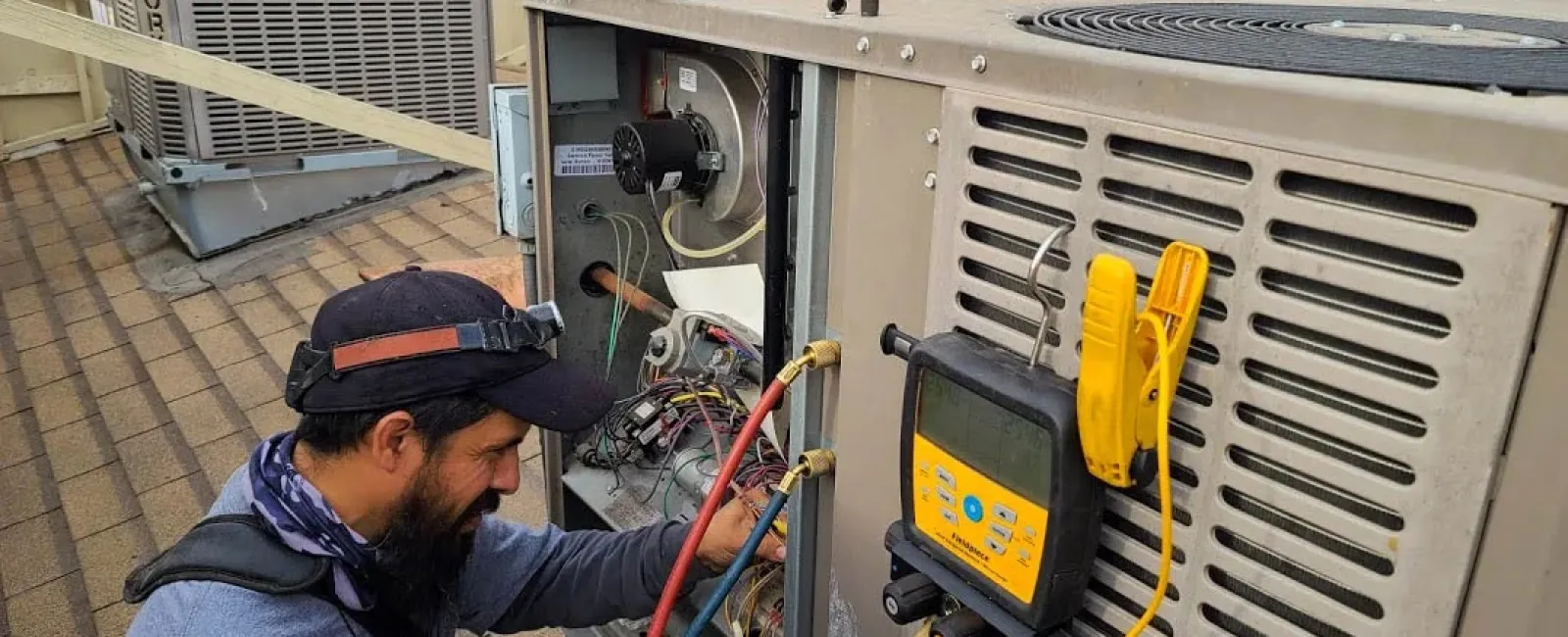 Technician inspecting and repairing rooftop HVAC unit with diagnostic tools and gauges during maintenance work.