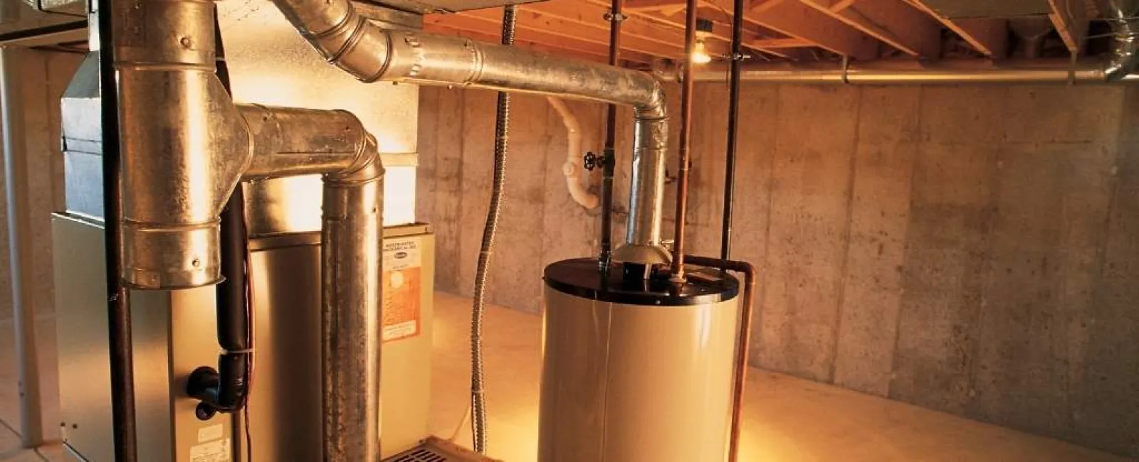 Basement room with water heater and furnace connected by metal ductwork and pipes under wooden ceiling.