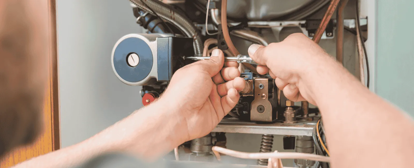 Technician using a tool to repair and adjust internal parts of a boiler or heating system.