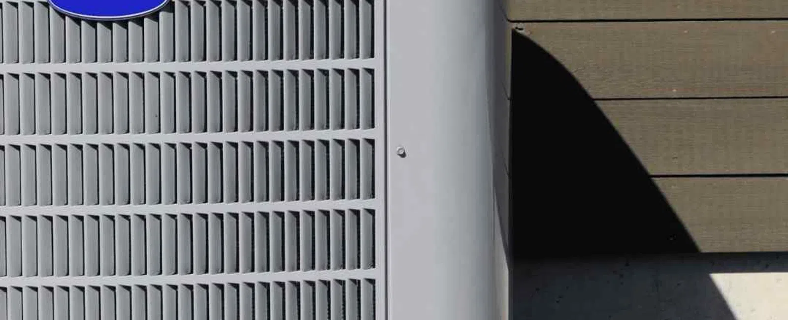 Gray outdoor air conditioning unit installed on concrete slab beside house with wooden siding.