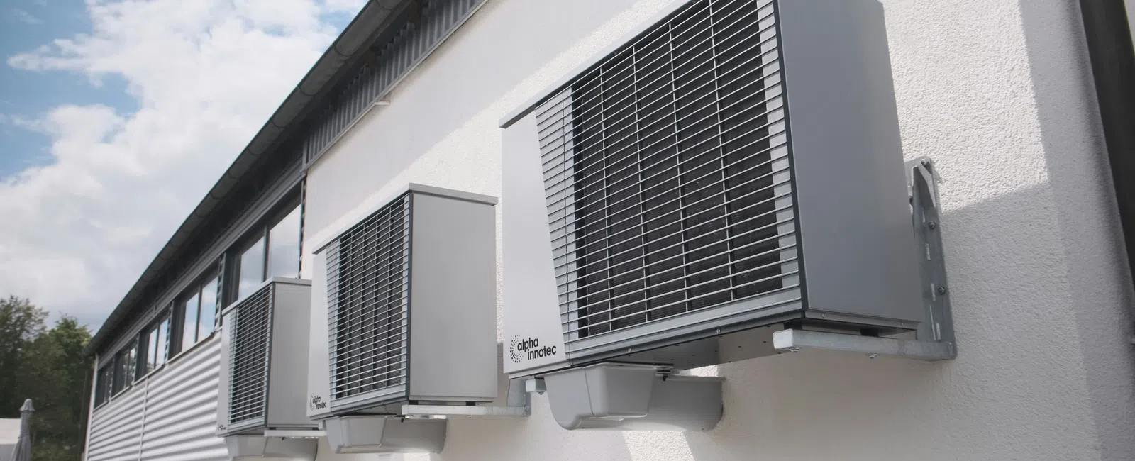 Three modern gray air conditioning units mounted on the exterior white wall of a commercial building.