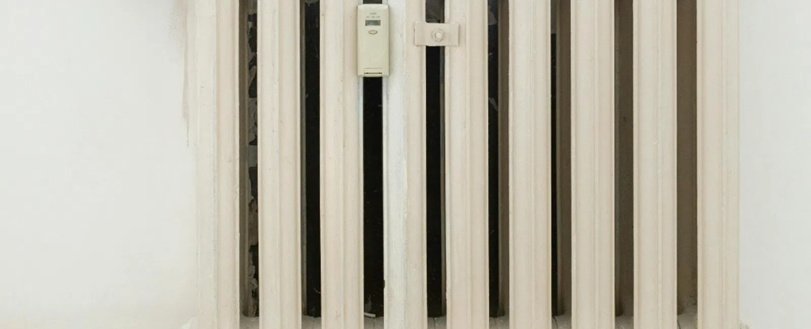 White metal radiator heater mounted on a wall with a temperature control valve on the left side