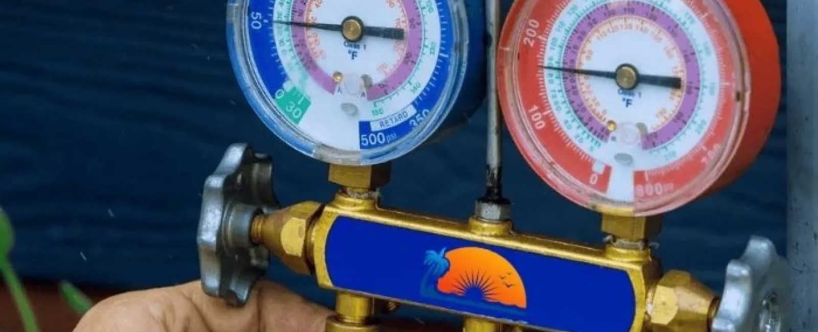 Close-up of a technician's hands holding HVAC manifold gauges with blue and red dials measuring pressure and temperature for AC refrigerant Torrance services.