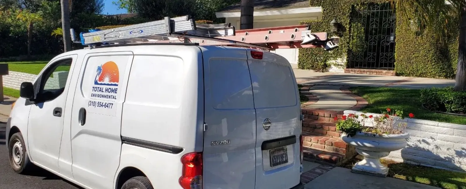 White service van with ladders on roof parked in front of residential home on sunny day