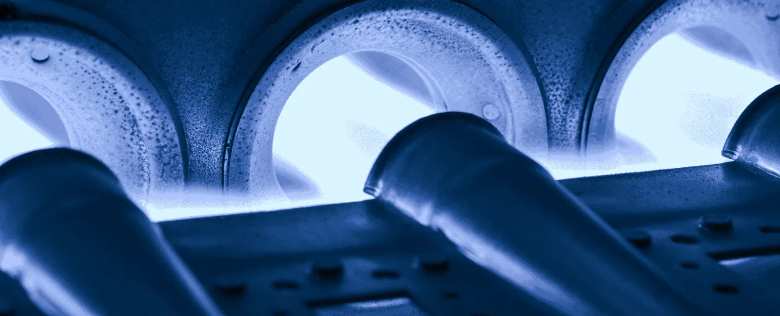 Close-up of blue natural gas flames burning inside a burner with metal pipes and perforated plate.