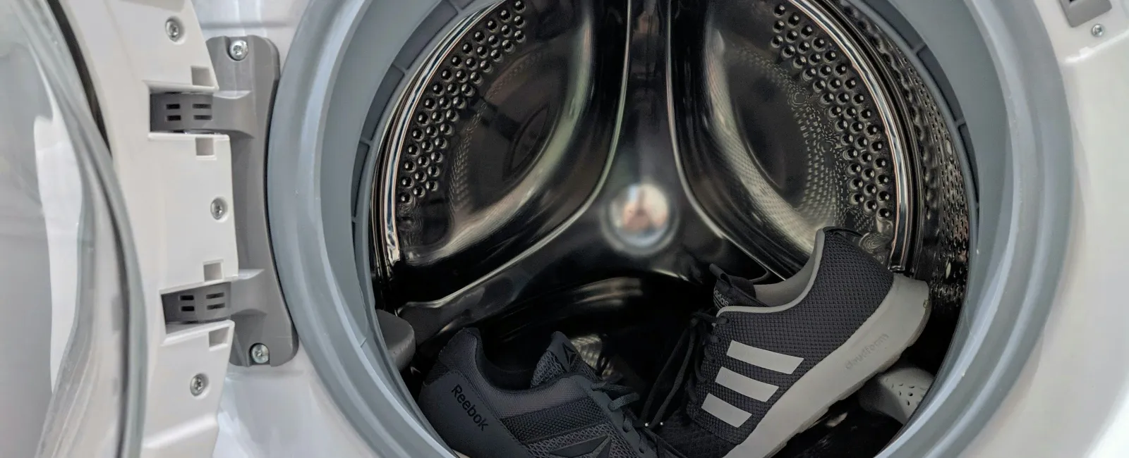 Black Reebok and Adidas sneakers inside the drum of an open front-loading washing machine