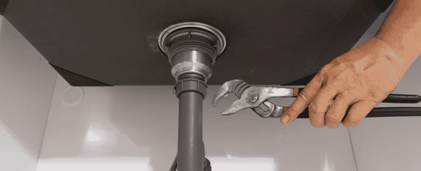 Hand using wrench to tighten or fix the plumbing pipe under a kitchen or bathroom sink.