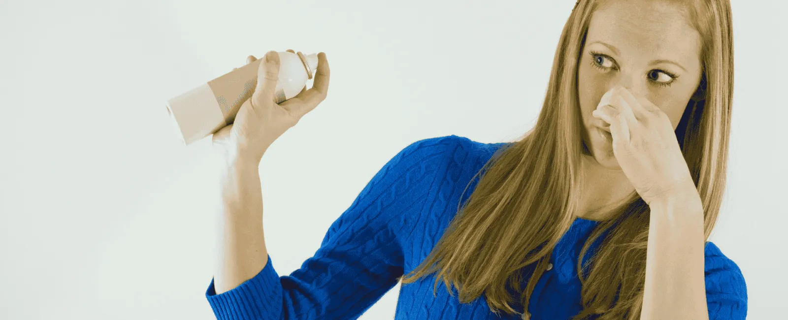 Woman in blue sweater pinching nose with one hand and holding spray can in other hand