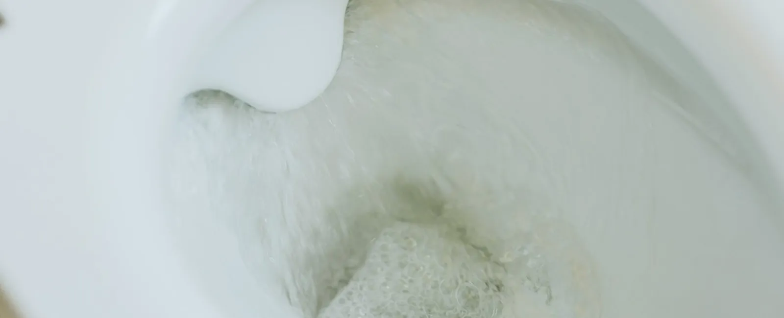 Close-up of a toilet bowl flushing with water swirling and bubbles inside the bowl.