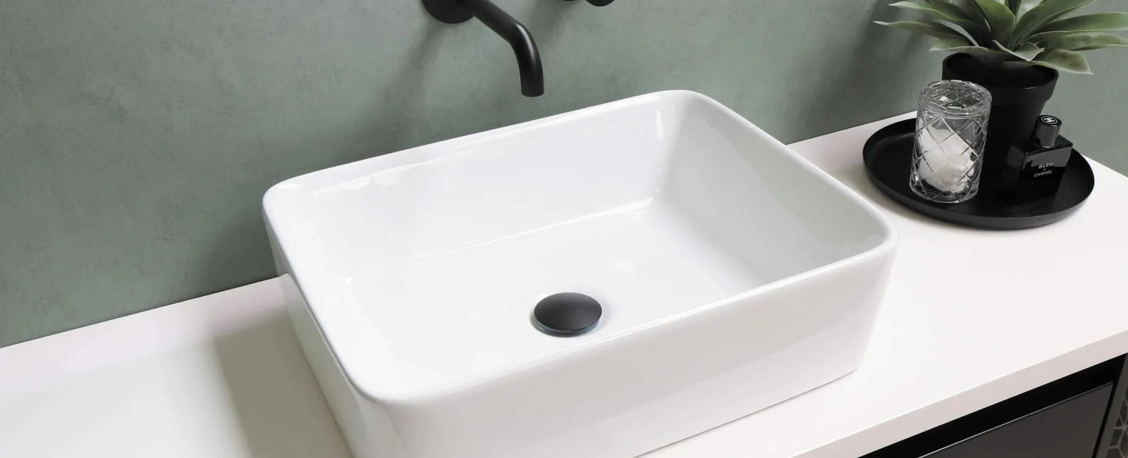 Modern rectangular white bathroom sink with matte black faucet and accessories on white countertop