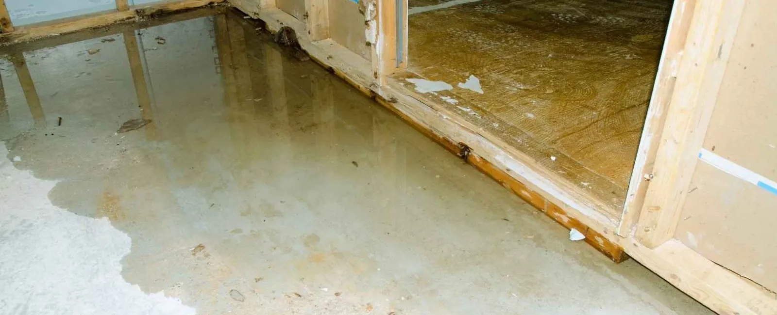 Water flooding an unfinished basement with exposed wooden framing and concrete floor
