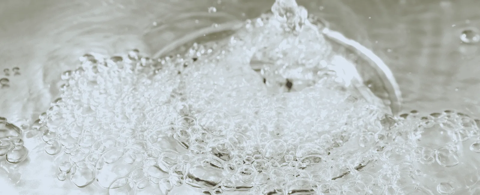 Close-up of clear water droplets and bubbles forming as water splashes on a smooth surface.