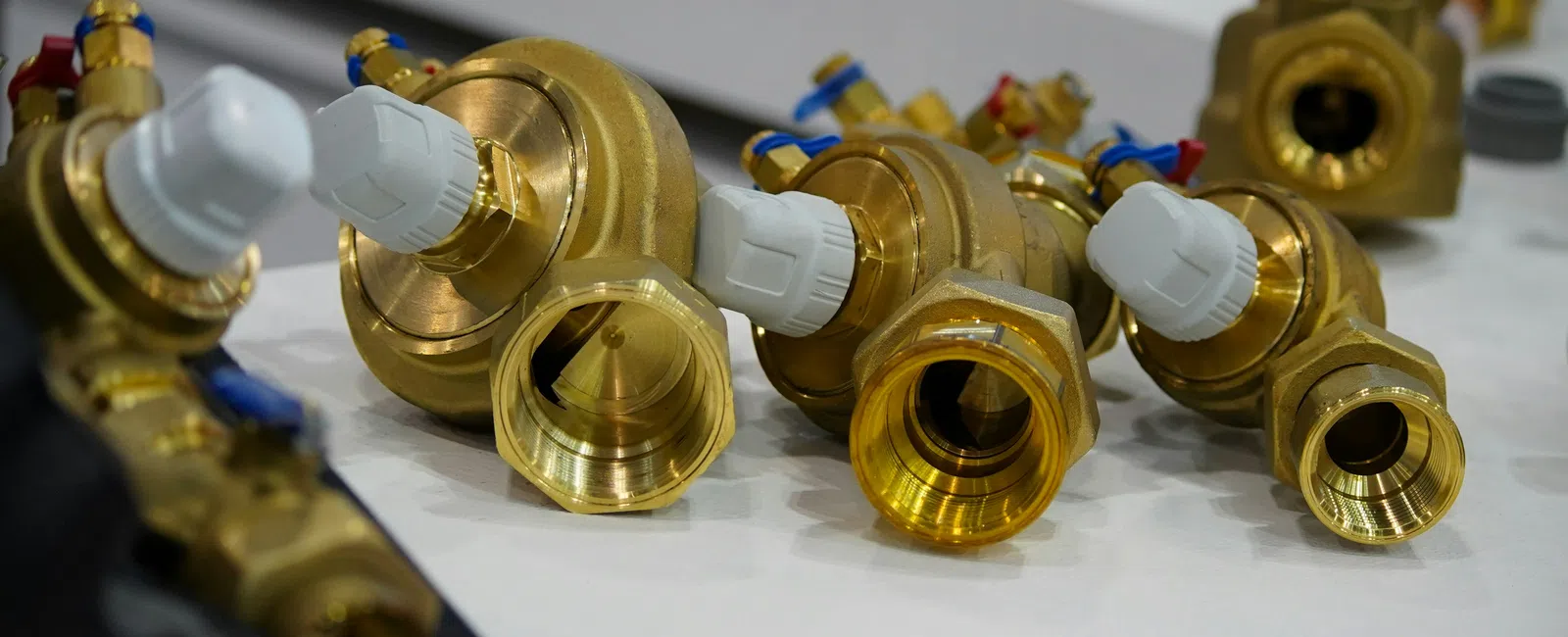 Close-up of multiple brass plumbing valves with white plastic handles arranged on a white surface.