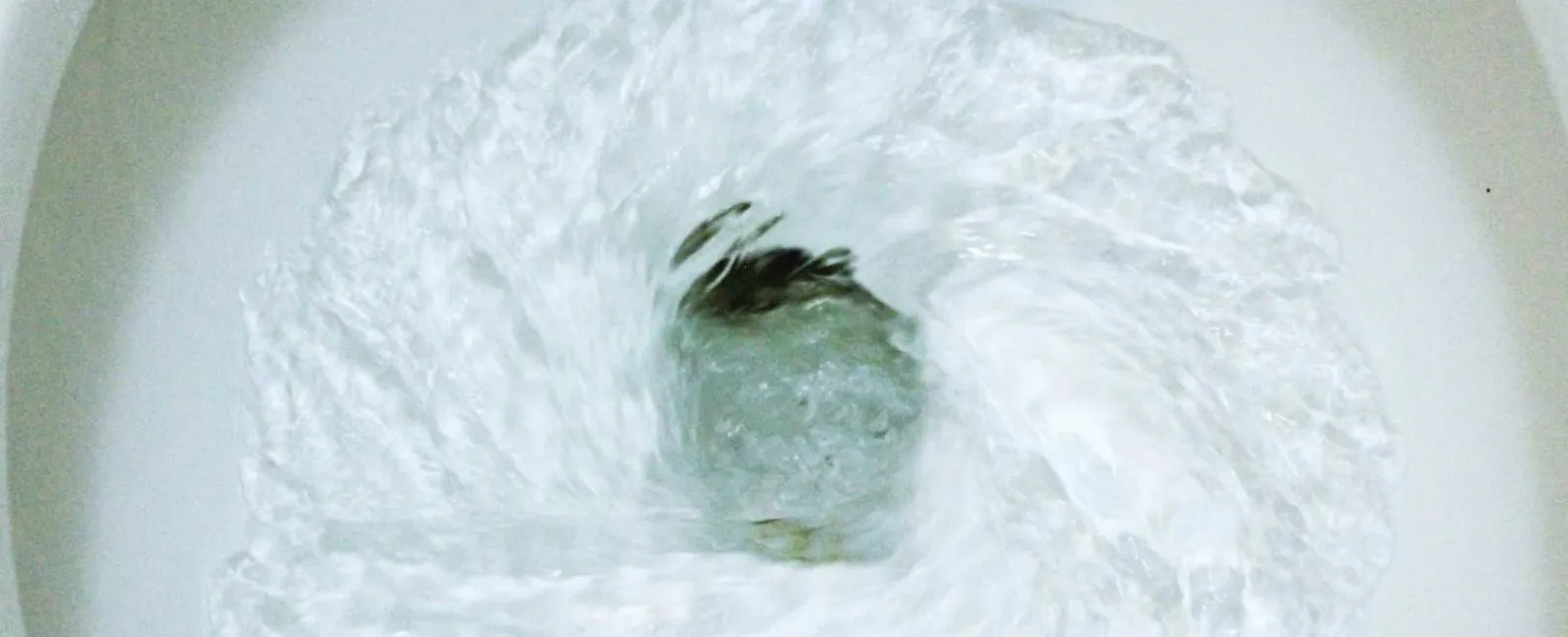 Water swirling rapidly down a white toilet bowl drain in a circular motion.