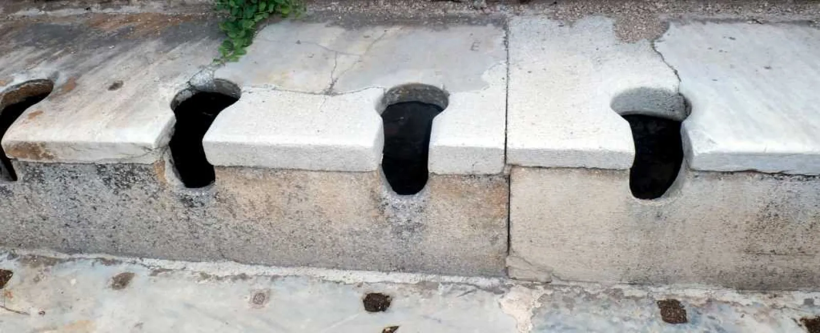 Ancient stone public toilets with partitioned seats and an old stone wall backdrop in historic site.