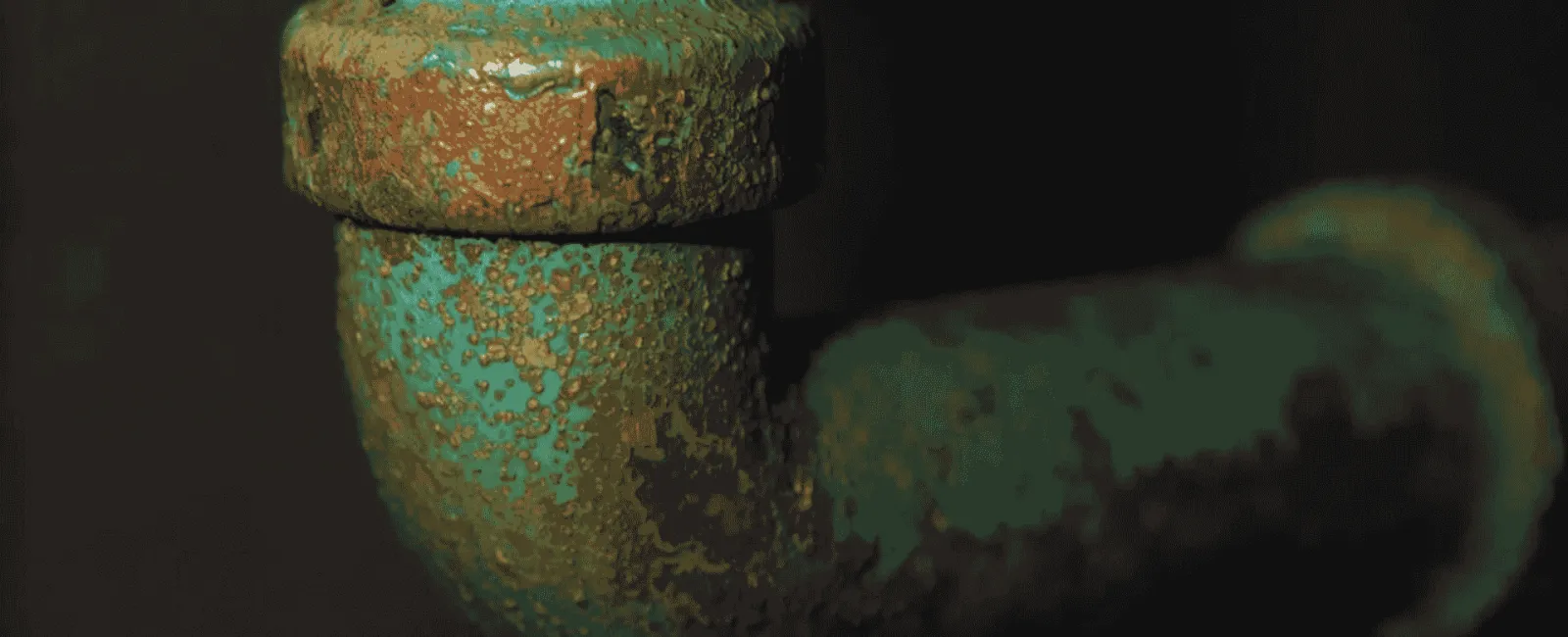 Close-up of a rusted, corroded metal pipe with green and brown oxidation against a dark background