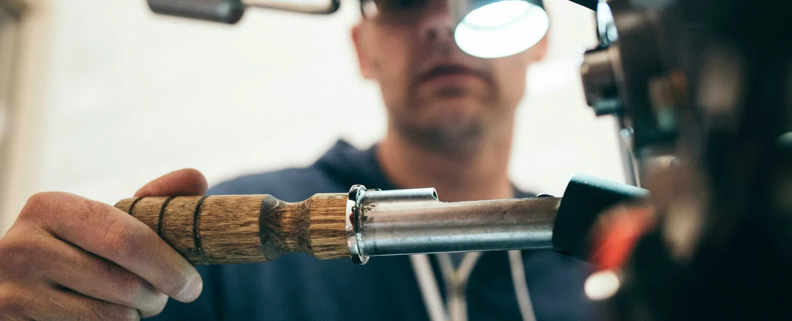 Barista using a wooden-handled portafilter to prepare espresso on a coffee machine.