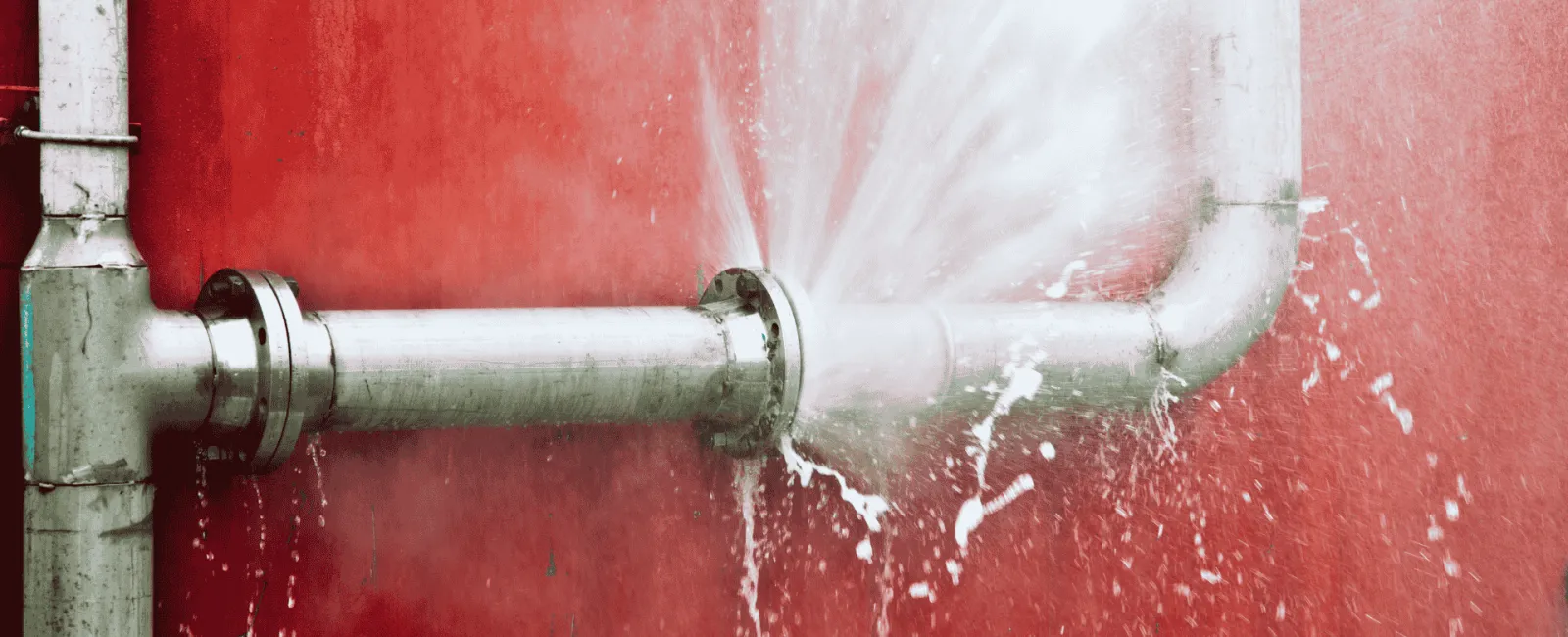 Water spraying from a burst pipe joint against a red wall, showing a plumbing leak issue.