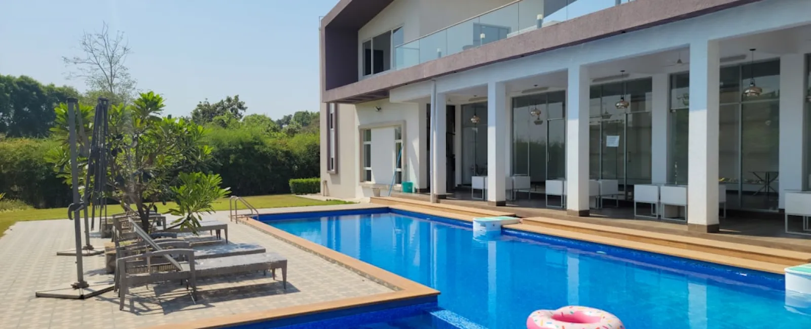 Modern house with large glass windows overlooking a blue swimming pool with lounge chairs and a pink inflatable ring