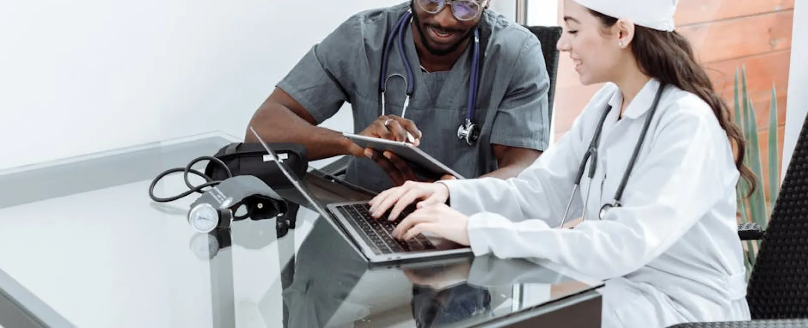Two doctors collaborating using a laptop and tablet in a modern office with medical tools on the table