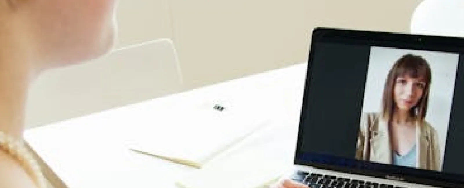 Woman wearing earphones video chatting with another woman on a laptop in a bright, modern room.