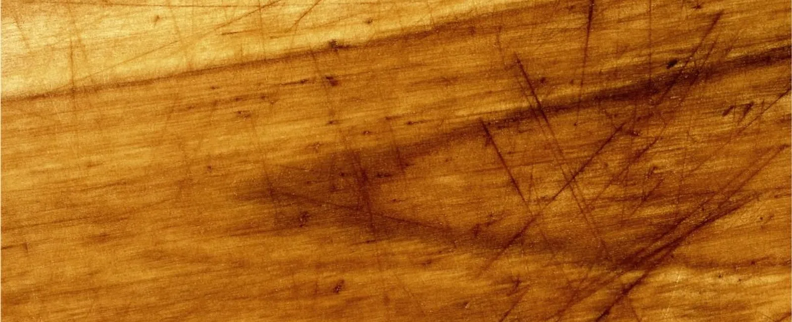 Close-up of a wooden surface with multiple scratches and natural wood grain texture in warm tones