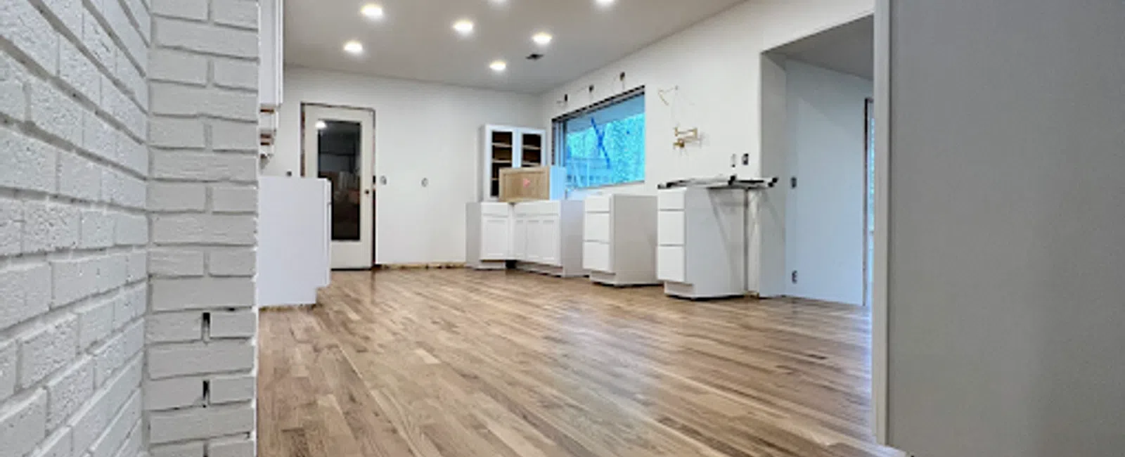 Spacious modern kitchen under construction with light wood flooring, white cabinets, and recessed ceiling lights.