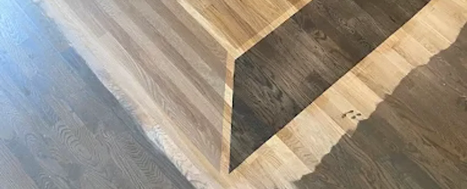 Wooden floor with a 3D illusion square design creating depth and shadow effects in a room corner.