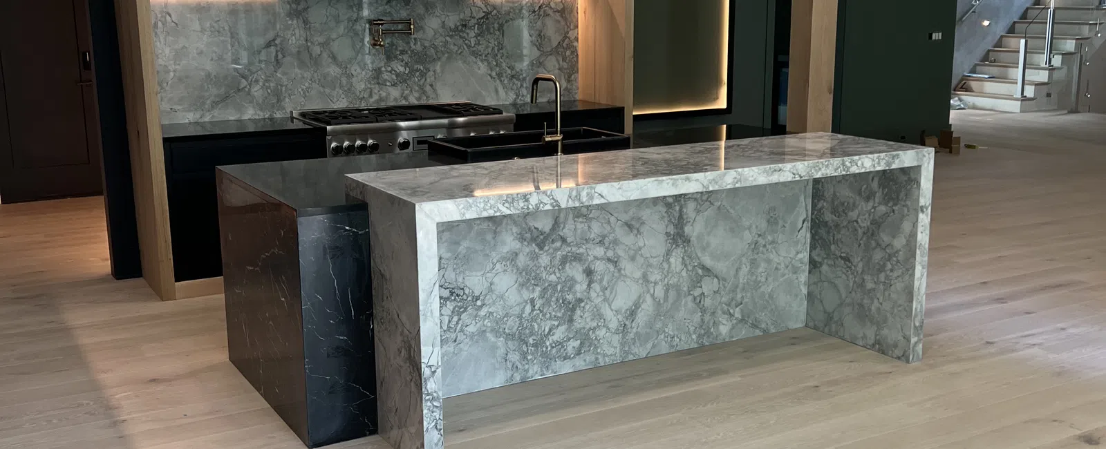 Modern kitchen with marble island, backlit cabinets, pendant lights, and light wood flooring in open space.