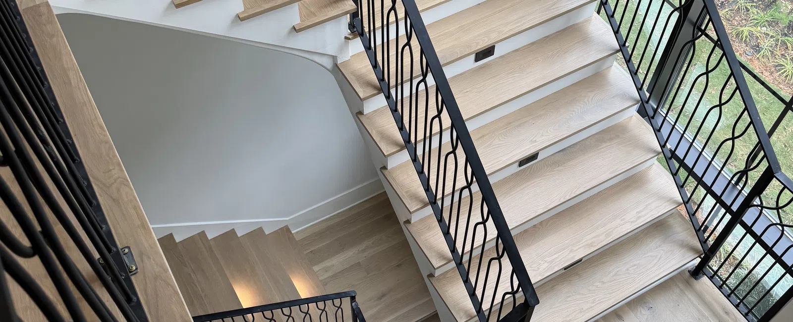 Modern wooden staircase with black metal railings inside a bright room with large windows