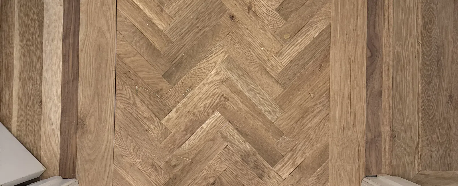 Person standing on newly installed herringbone wood floor with tools laid out, door frames visible on sides.