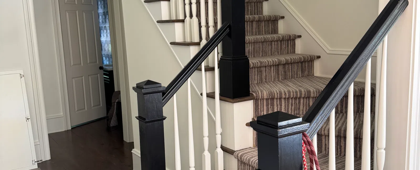 Interior staircase with dark wood handrails, white balusters, and striped carpet runner in a bright home.