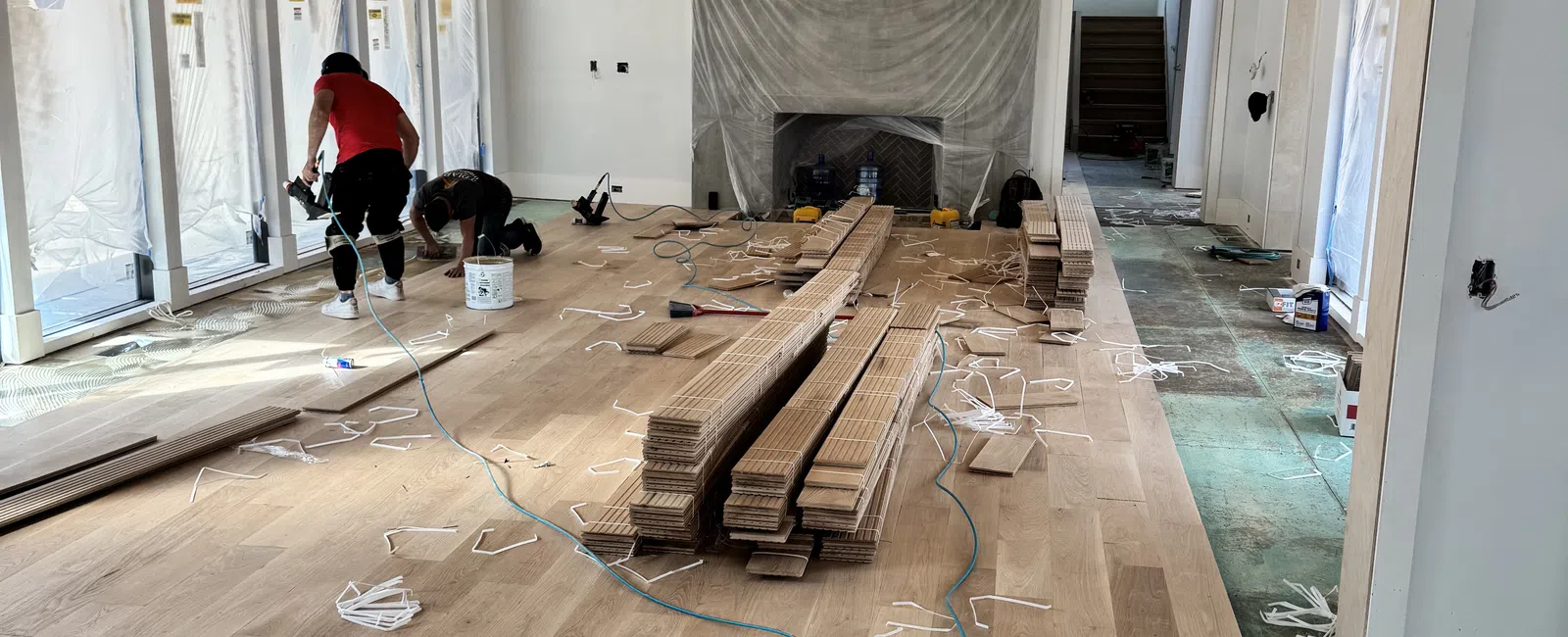 Workers installing wooden flooring in a spacious room with vaulted wood ceiling and covered fireplace.