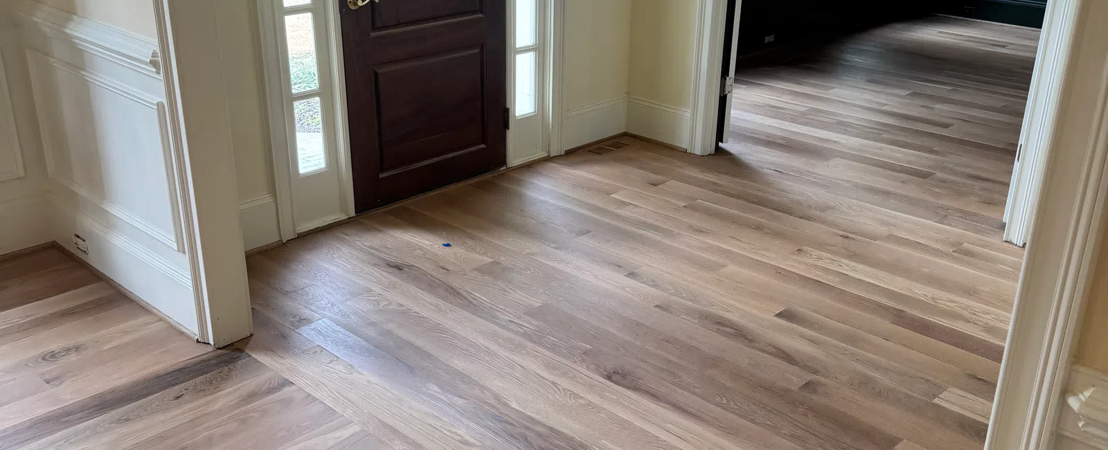 Entryway with dark wood front door, arched transom window, and light-toned hardwood floors in a bright home.