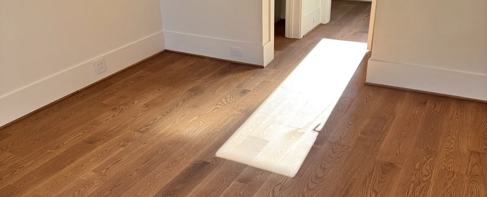 Sunlight streaming through doorway onto hardwood floor in empty room with white walls and open closets