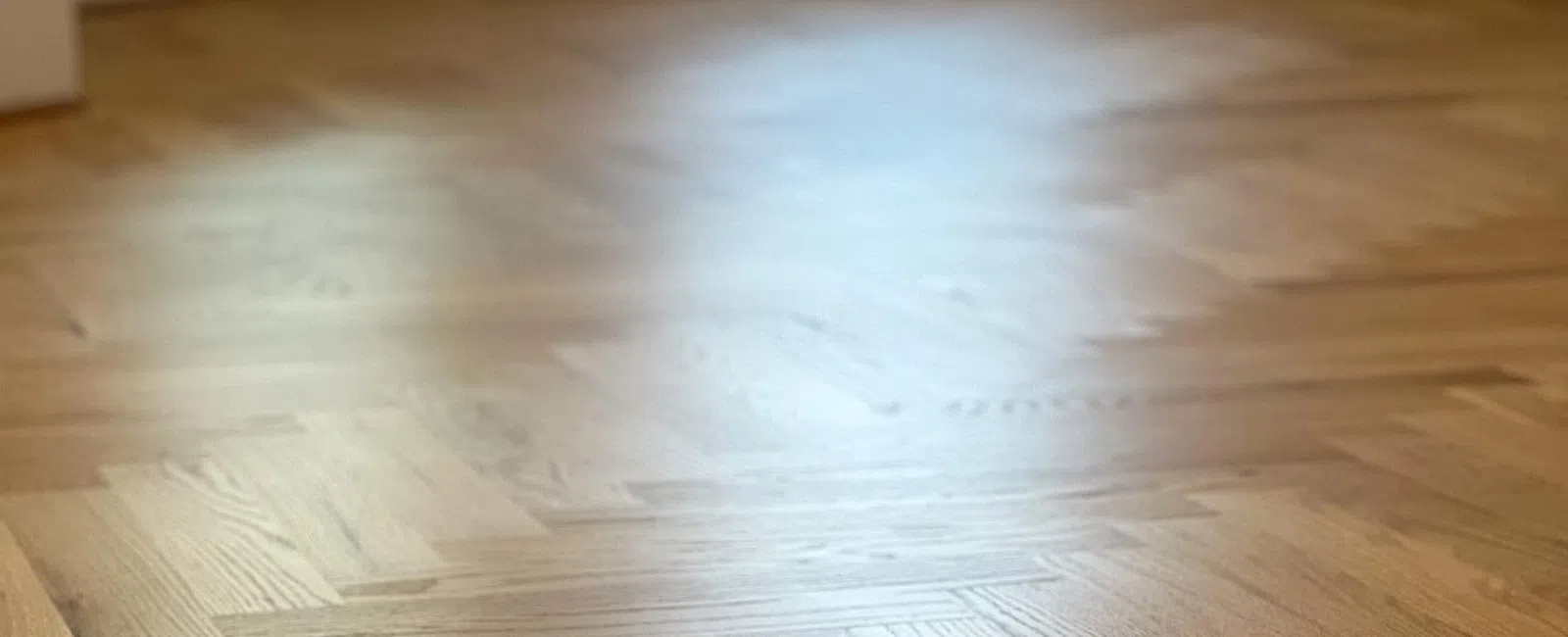Close-up of smooth, polished hardwood floor with herringbone pattern in a bright room.