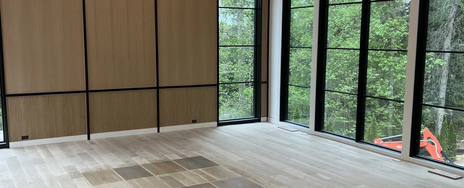 Modern bright room with large black-framed windows, wood floor samples, and an elegant chandelier under arched ceiling.