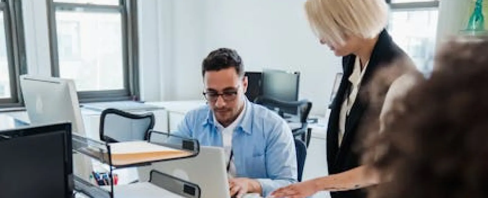 Team of software developers collaborating in a bright office, coding and discussing work at computers.