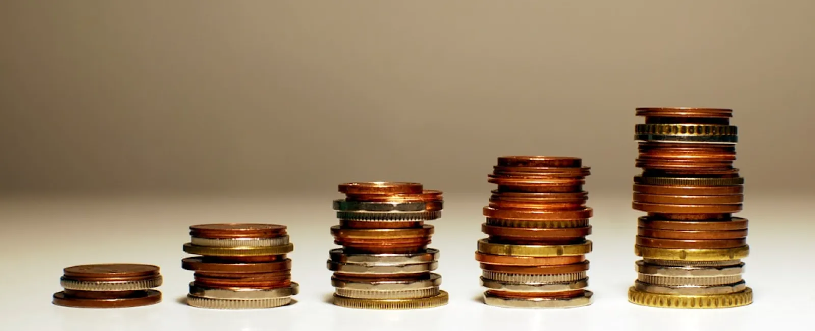 Stacks of mixed coins arranged in ascending order on a reflective surface with a neutral background