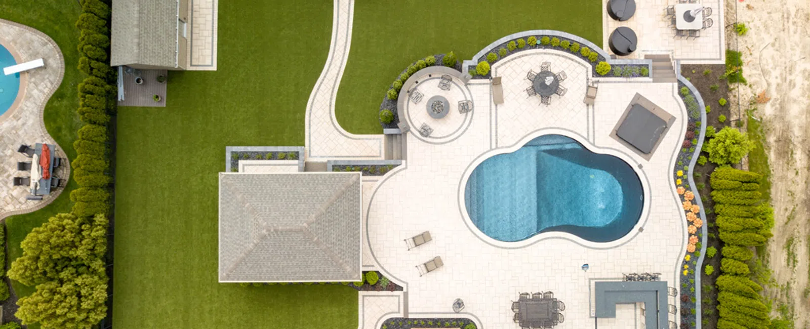 Aerial view of a backyard with a kidney-shaped pool, patio, seating areas, green lawn, and docked boats.
